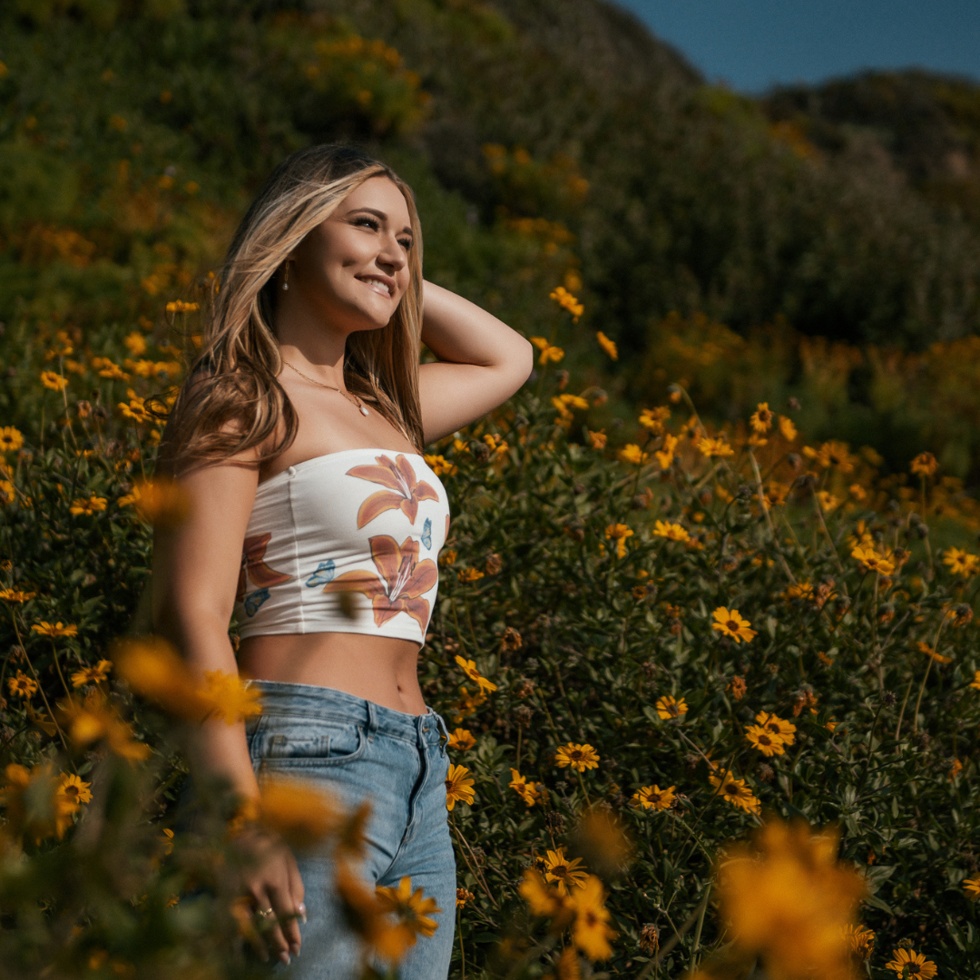 teen blond girl in sunlight wearing a tube top and blue jeans, smiling off to the side while in a field of orange wildflowers at westward beach in malibu for her senior portraits