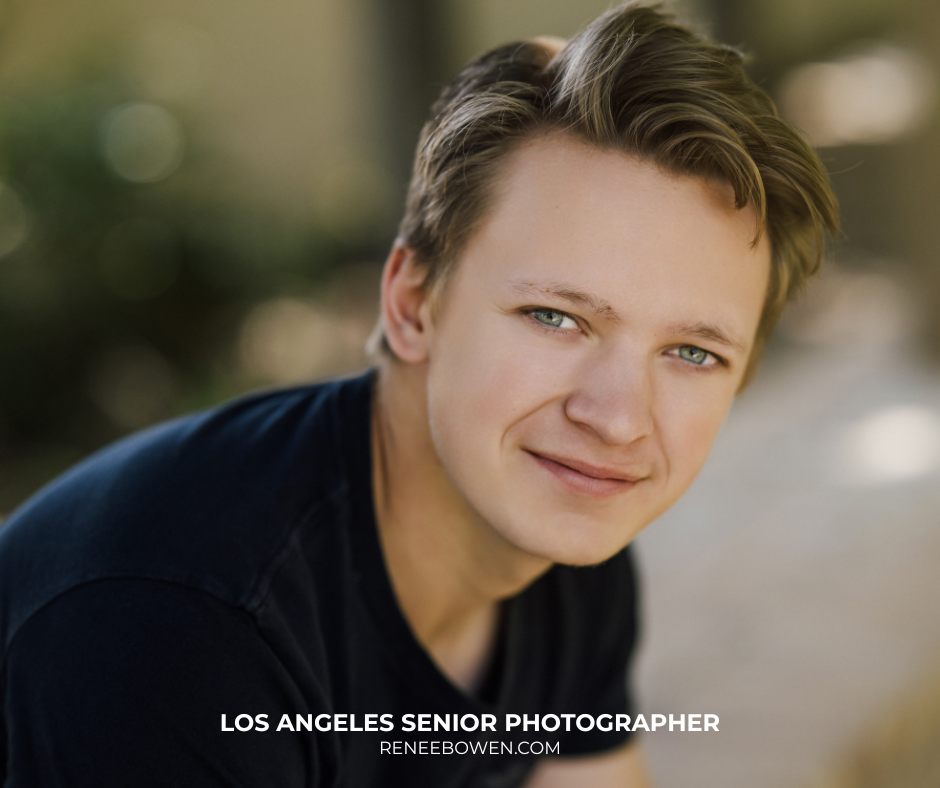close up senior portrait of a teen boy with short blond hair and blue eyes where he is sitting down leaning forward and wearing a blue shirt with a soft smile